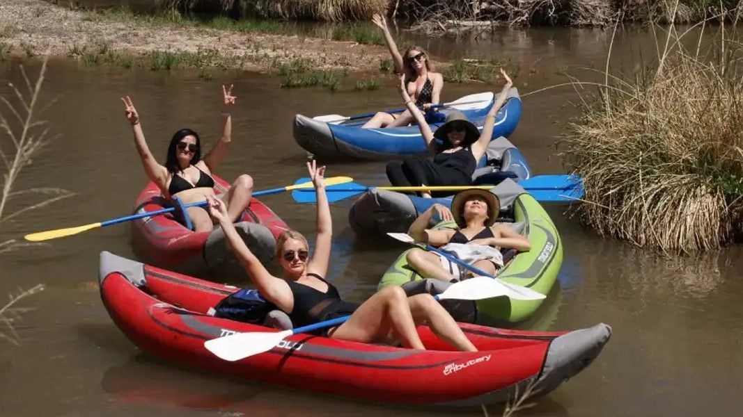 Five people in inflatable kayaks on a river, arms raised in celebration.