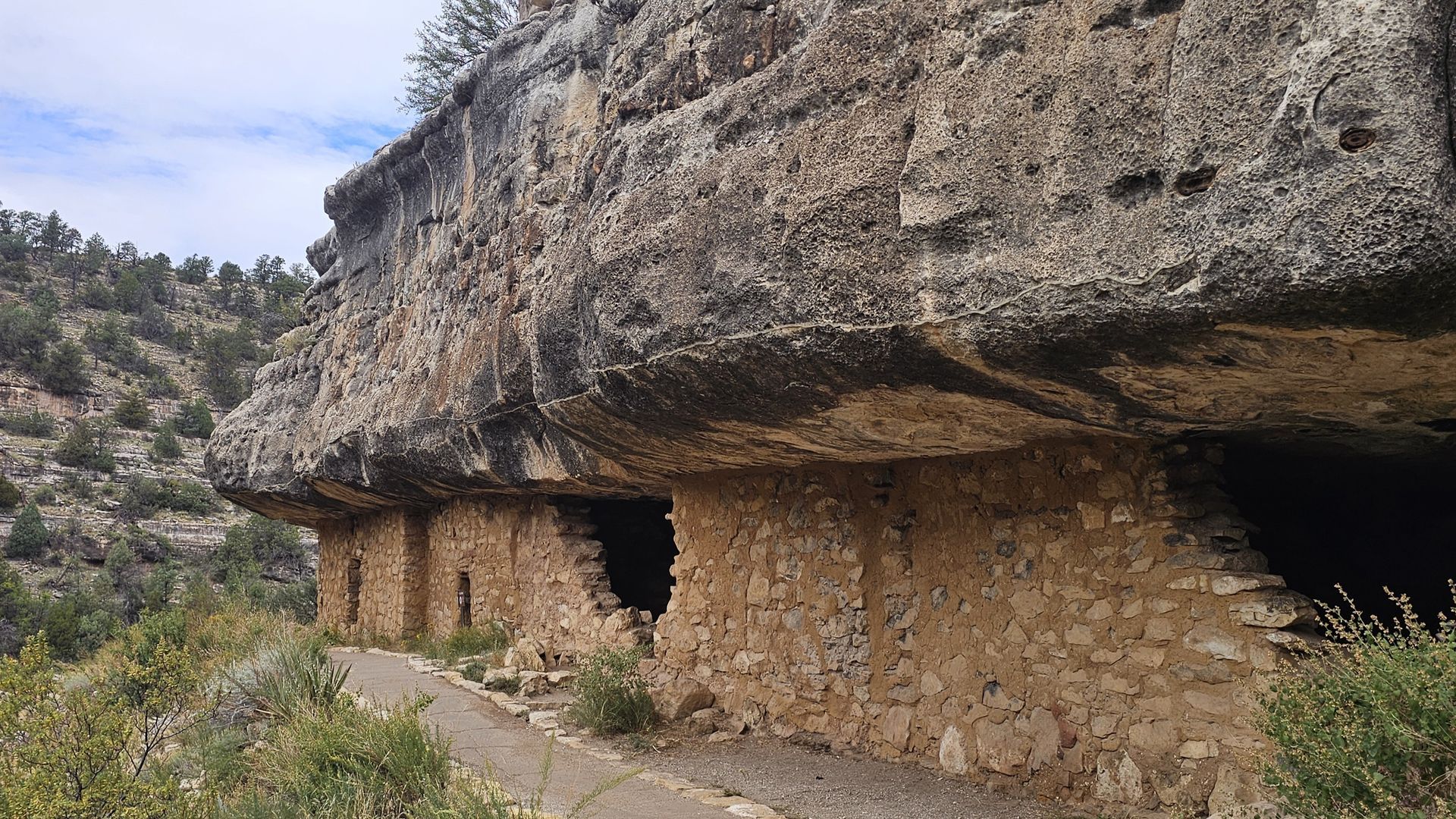 Cliff dwellings built into a rock overhang, with a path leading to them.