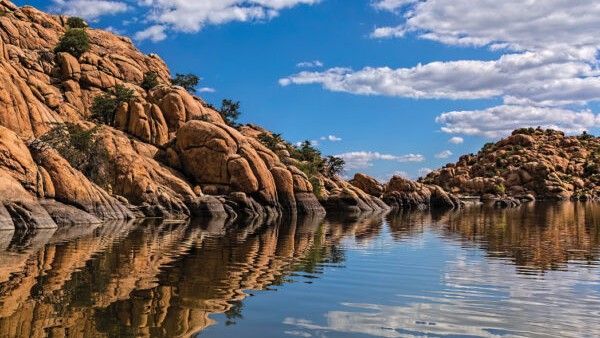 Rocky cliffs reflected in calm water, under a blue sky with fluffy white clouds.
