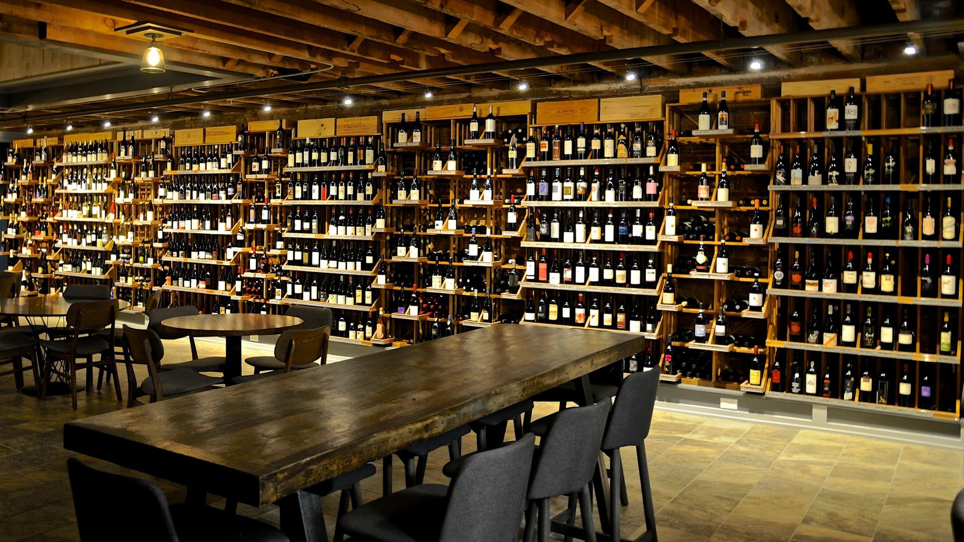 Wine bottles on shelves in a dimly lit room; tables and chairs for seating.