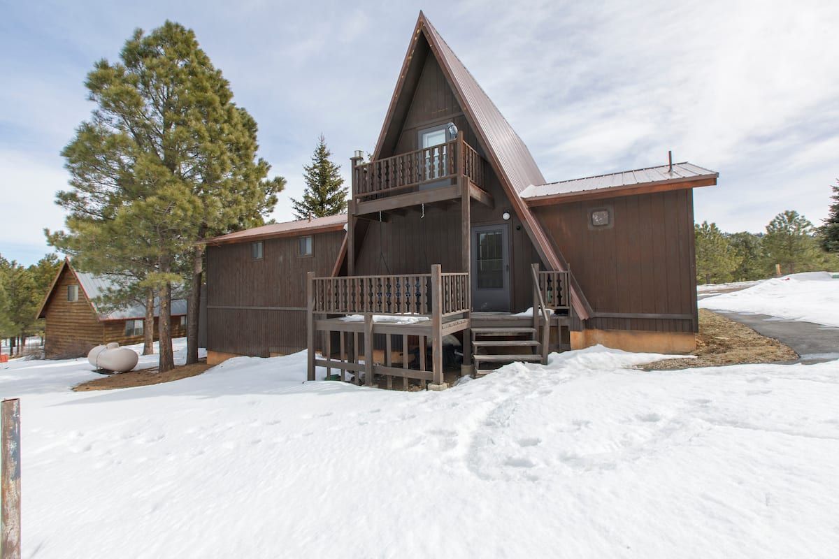 A small a frame cabin in the snow with trees in the background