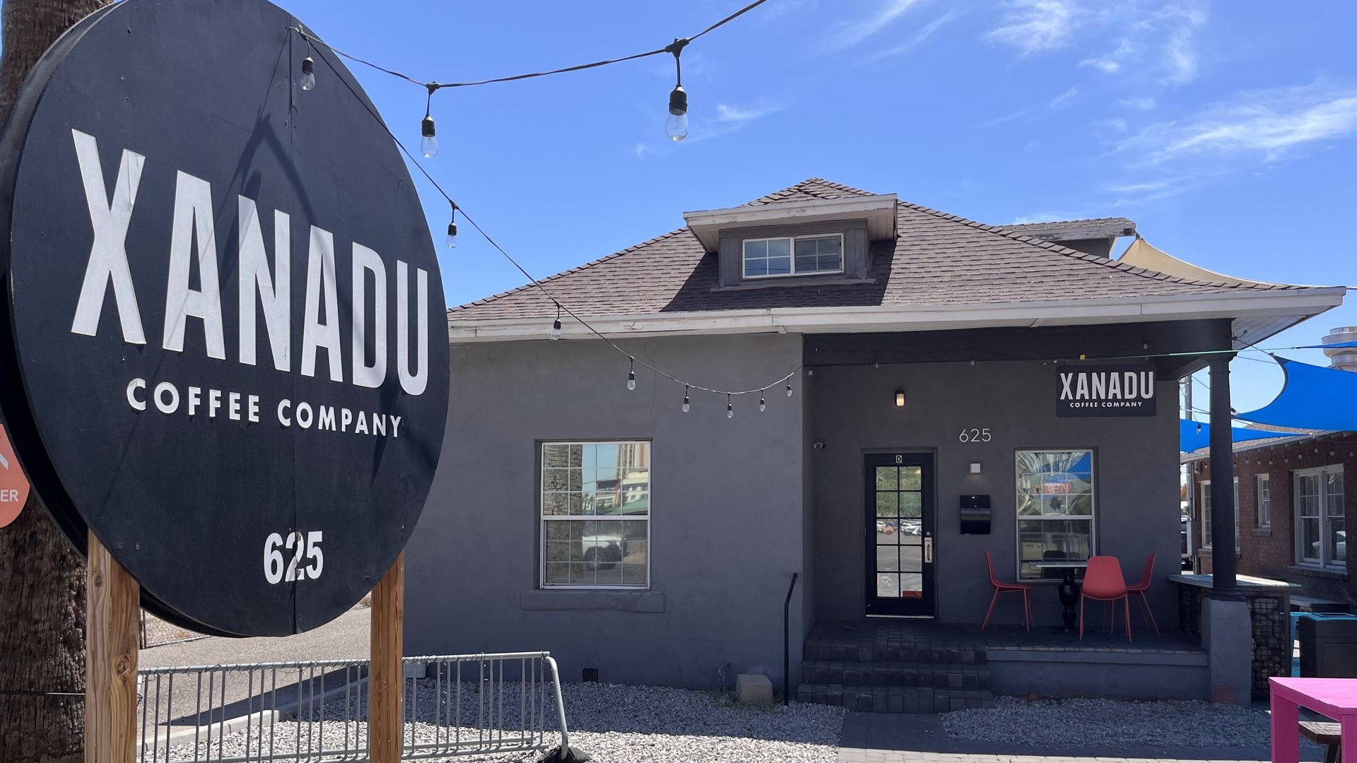 Xanadu Coffee Company sign and building exterior. Black sign, gray building, string lights, patio seating.