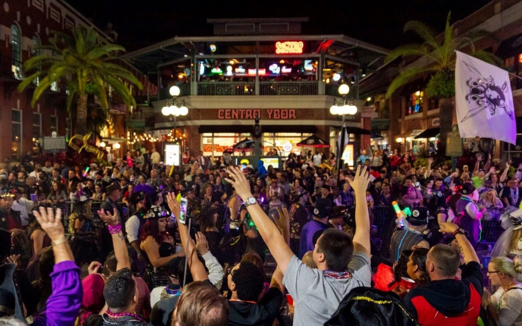 Nighttime crowd at a Central Florida entertainment district with people waving their arms and enjoying a festive atmosphere.