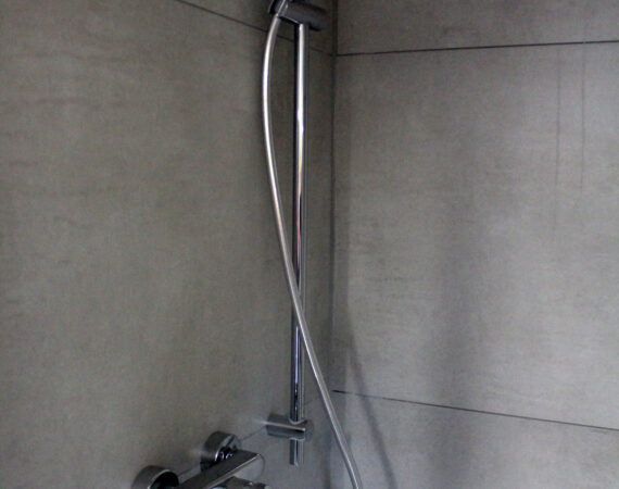 Dusche mit silberfarbenen Armaturen vor hellgrauer Fliesenwand.