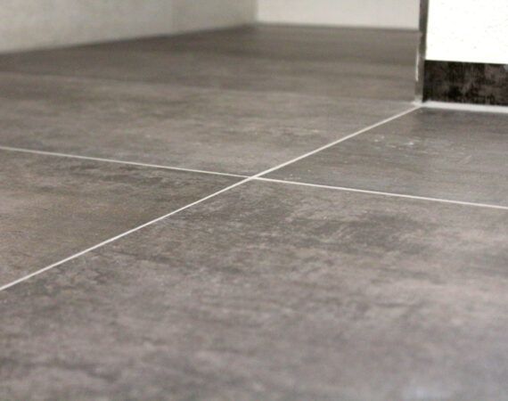 Grauer Keramikfliesenboden mit weißen Fugen.