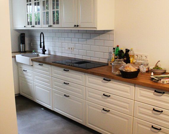 Weiße Küche mit weißen Schränken, dunklen Arbeitsplatten und schwarzem Wasserhahn.