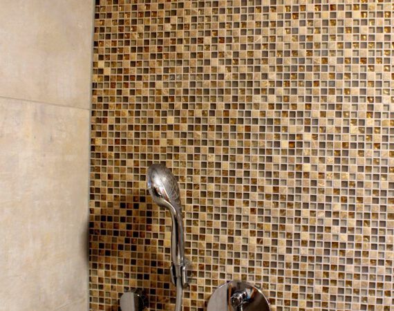 Dusche mit Mosaikfliesenwand und silberner Duschkopfarmatur.