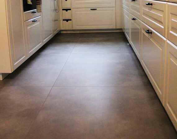 Grauer Fliesenboden in der Küche zwischen weißen Schränken.