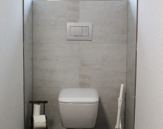 Modernes, wandhängendes WC in einer kleinen Nische mit grau gefliesten Wänden.