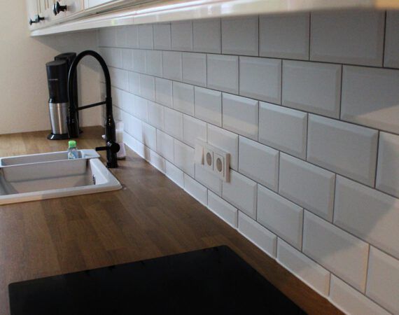 Küchenrückwand mit weißen Metrofliesen, Arbeitsplatte aus Holz und schwarzer Armatur.