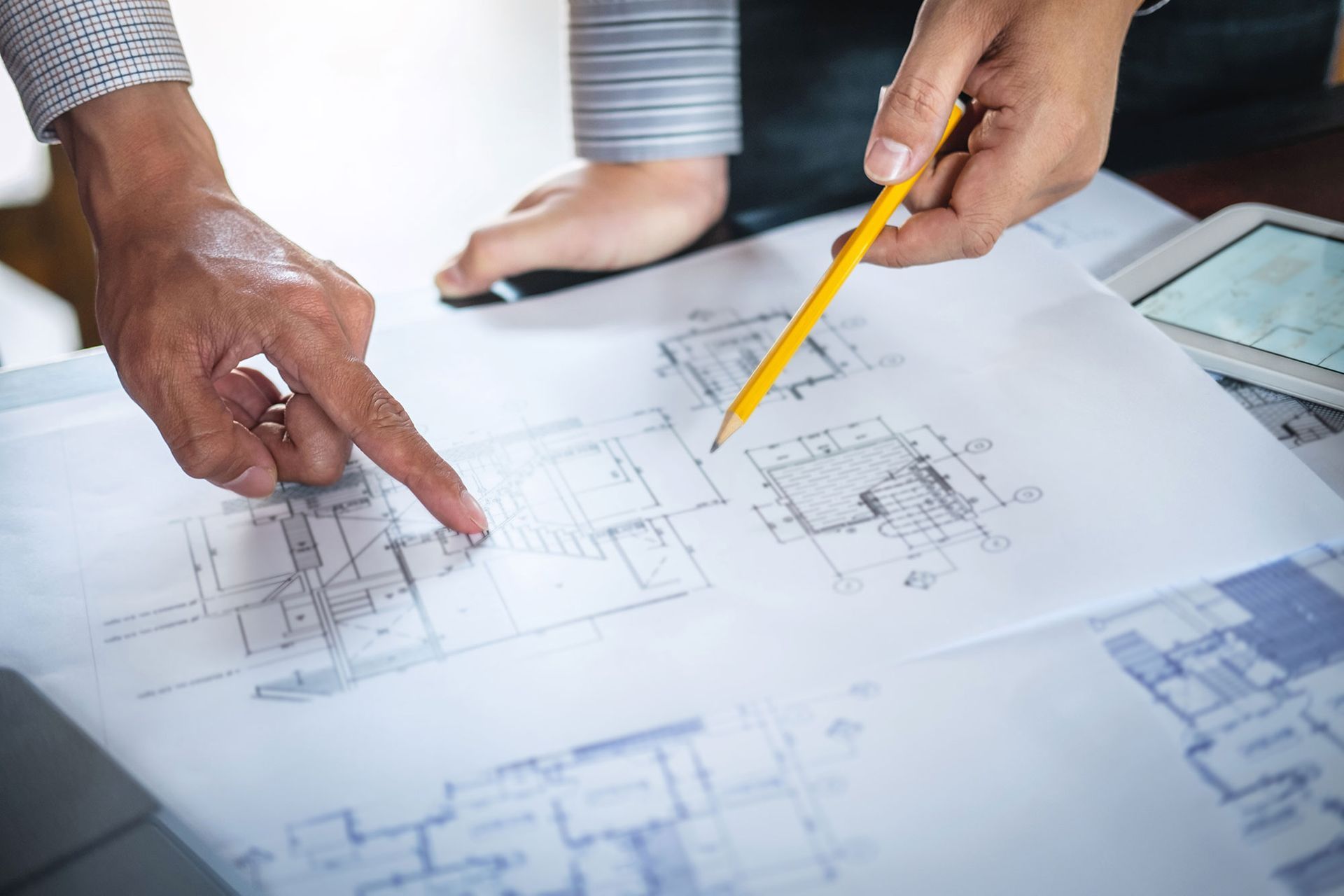 Hände zeigen auf Architekturpläne, Entwürfe werden mit einem Bleistift besprochen.