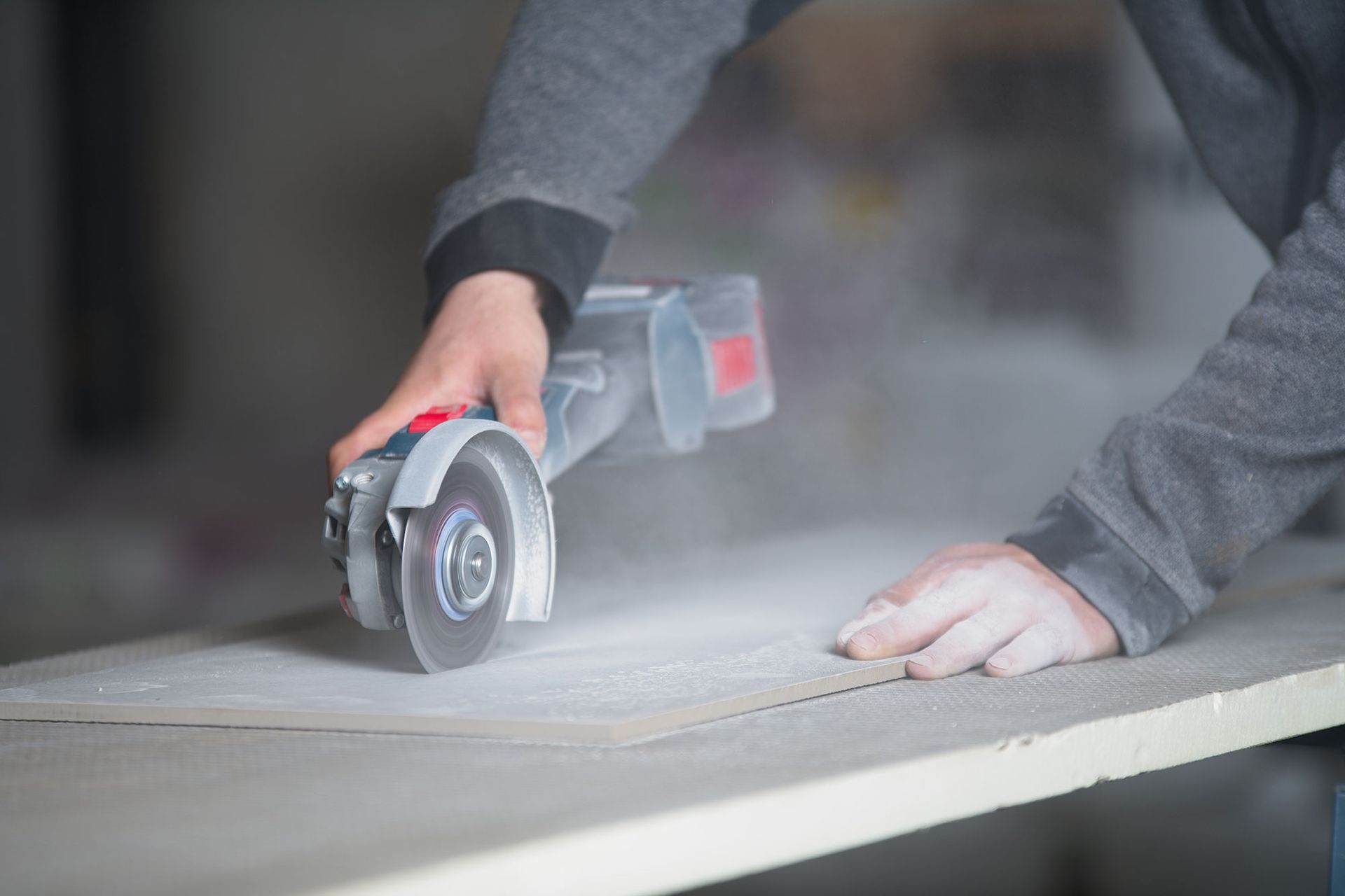Eine Person benutzt einen Winkelschleifer, um ein helles Brett zu schneiden und erzeugt dabei Staub.