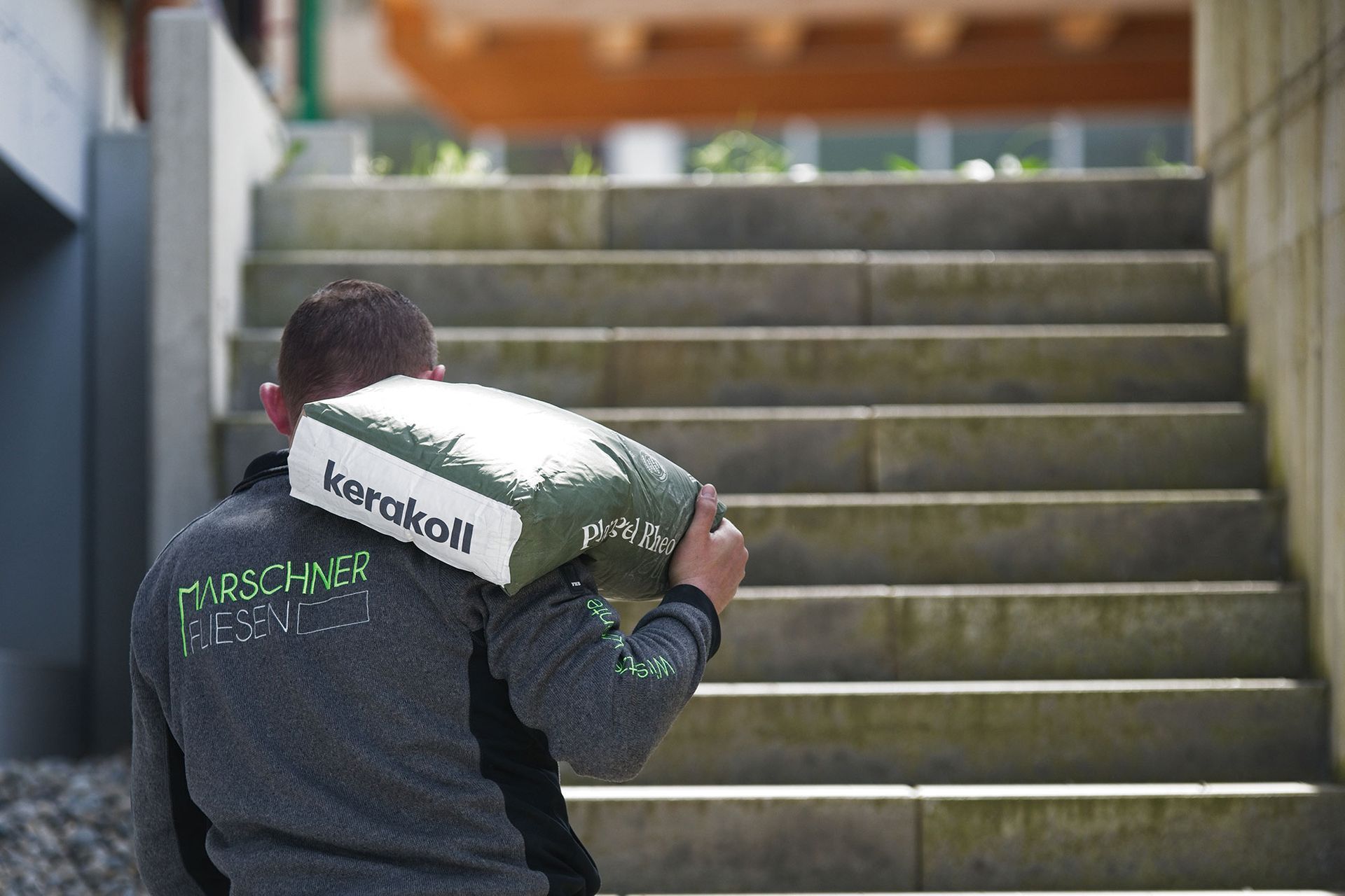 Ein Mann trägt eine mit „kerakoll“ beschriftete Tasche eine Außentreppe aus Stein hinauf.