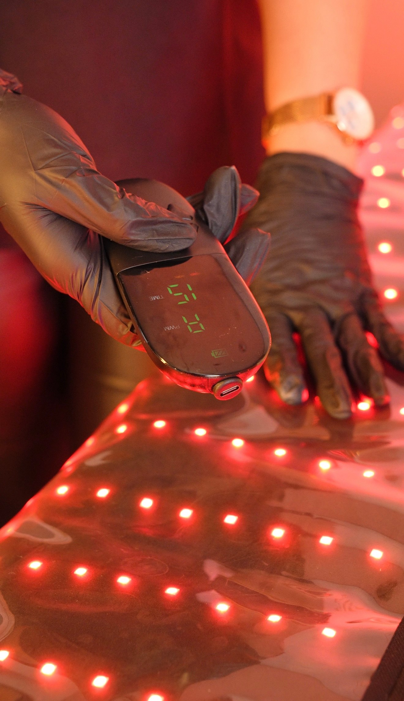 Manos enguantadas sosteniendo un pequeño dispositivo sobre una superficie iluminada en rojo con luces LED brillantes.