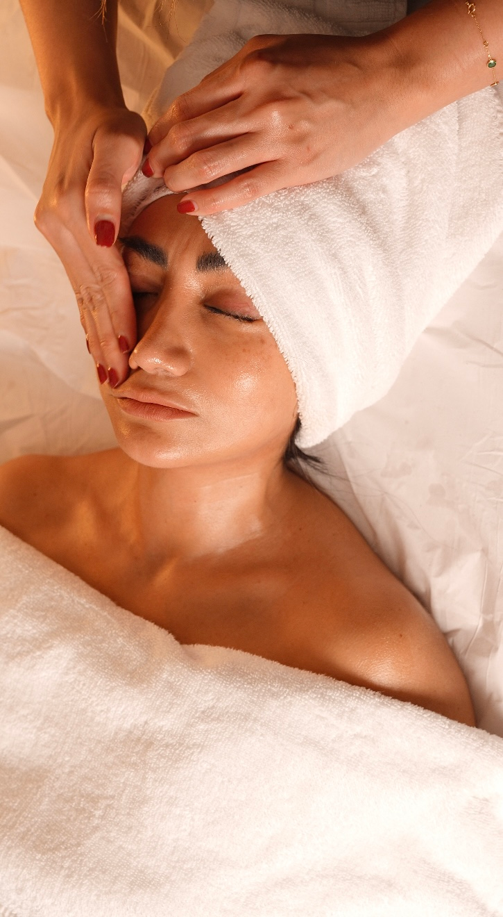 Mujer recibiendo un masaje facial con una toalla envuelta alrededor de la cabeza en un entorno de spa.
