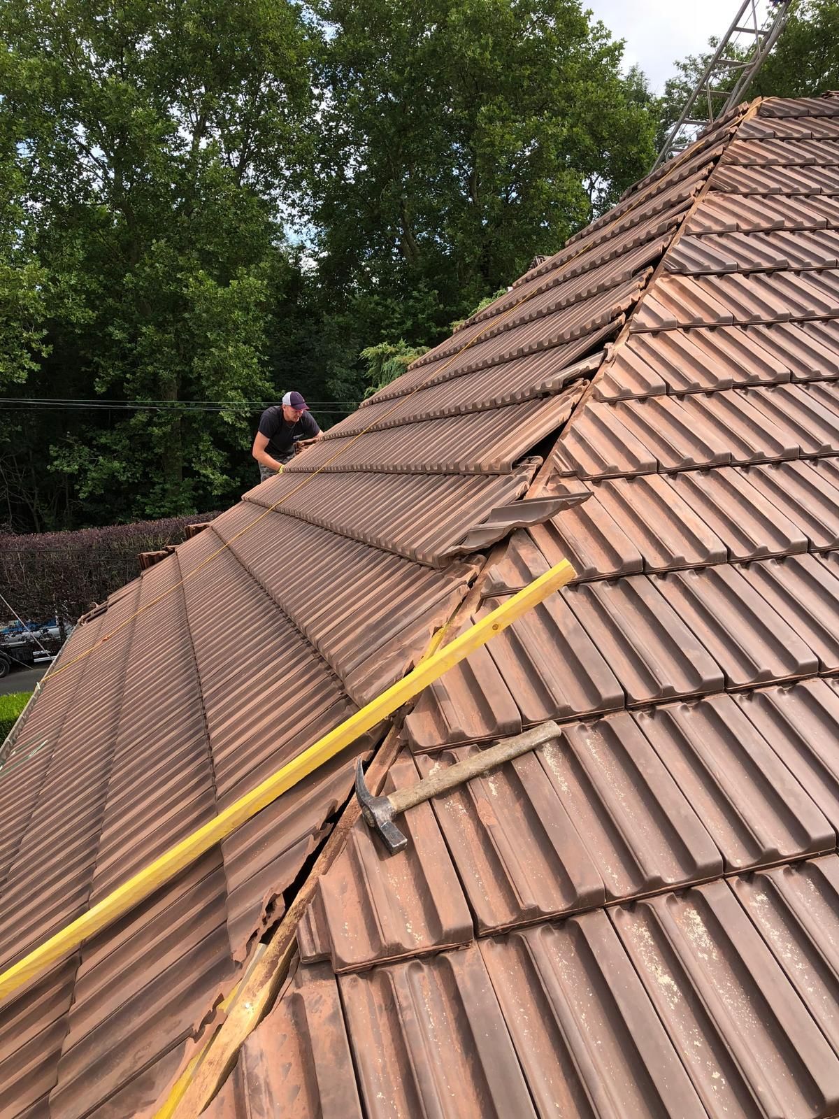 Des ouvriers fixent une longue sangle jaune sur un toit de tuiles, avec des arbres en arrière-plan.