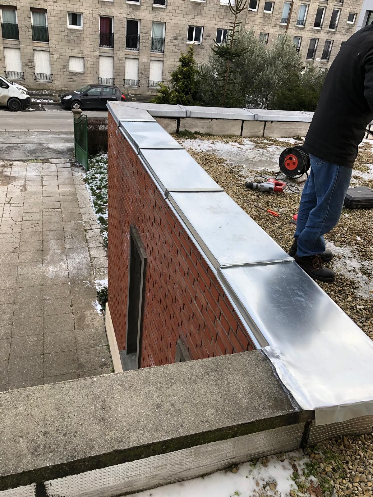 Toit recouvert de gravier et de murs en briques ; une personne se tient près du bord, à côté d'une brouette rouge.