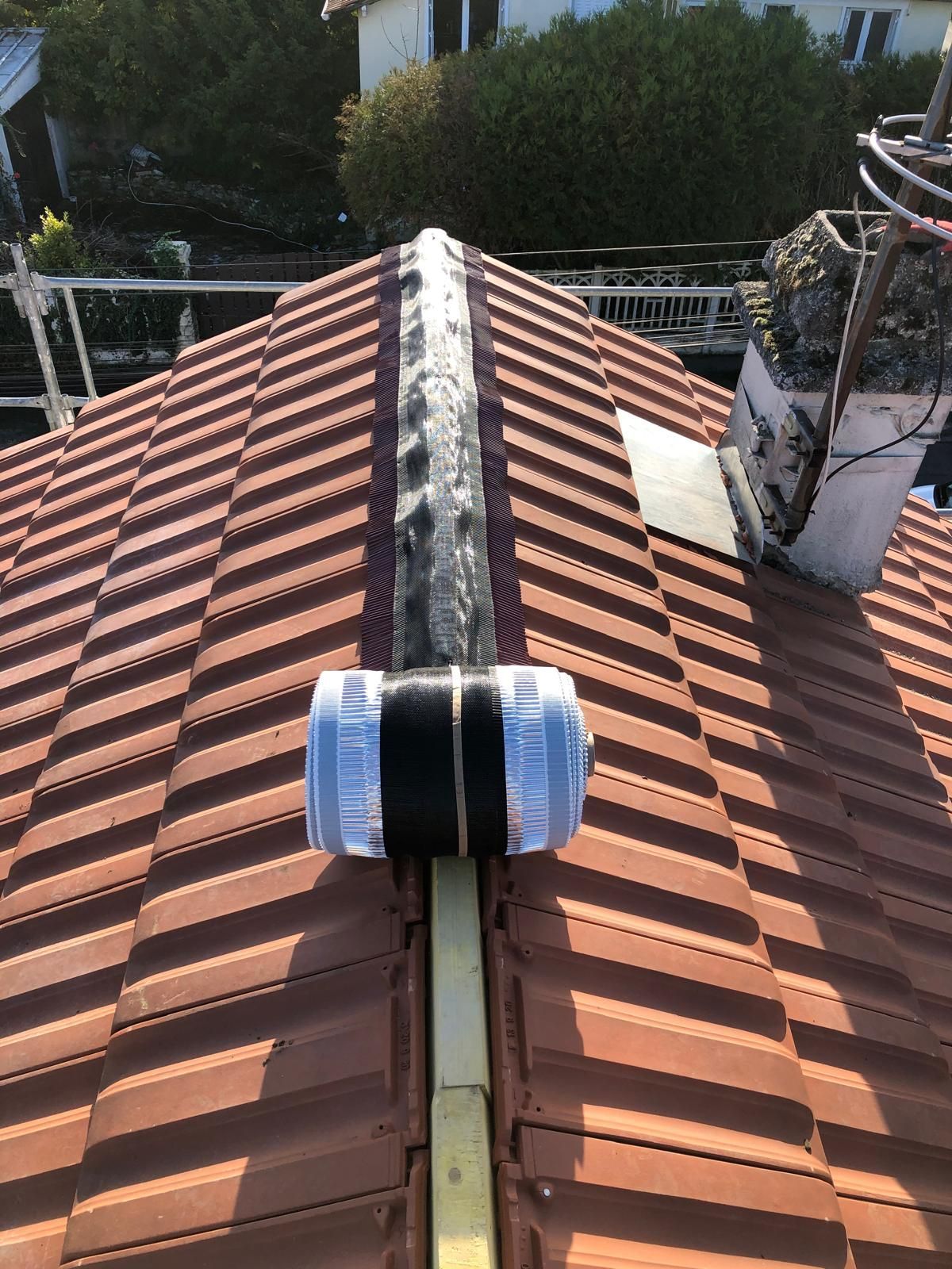 Faîtage en tuiles de terre cuite et chapeau de ventilation noir sur un toit ensoleillé.