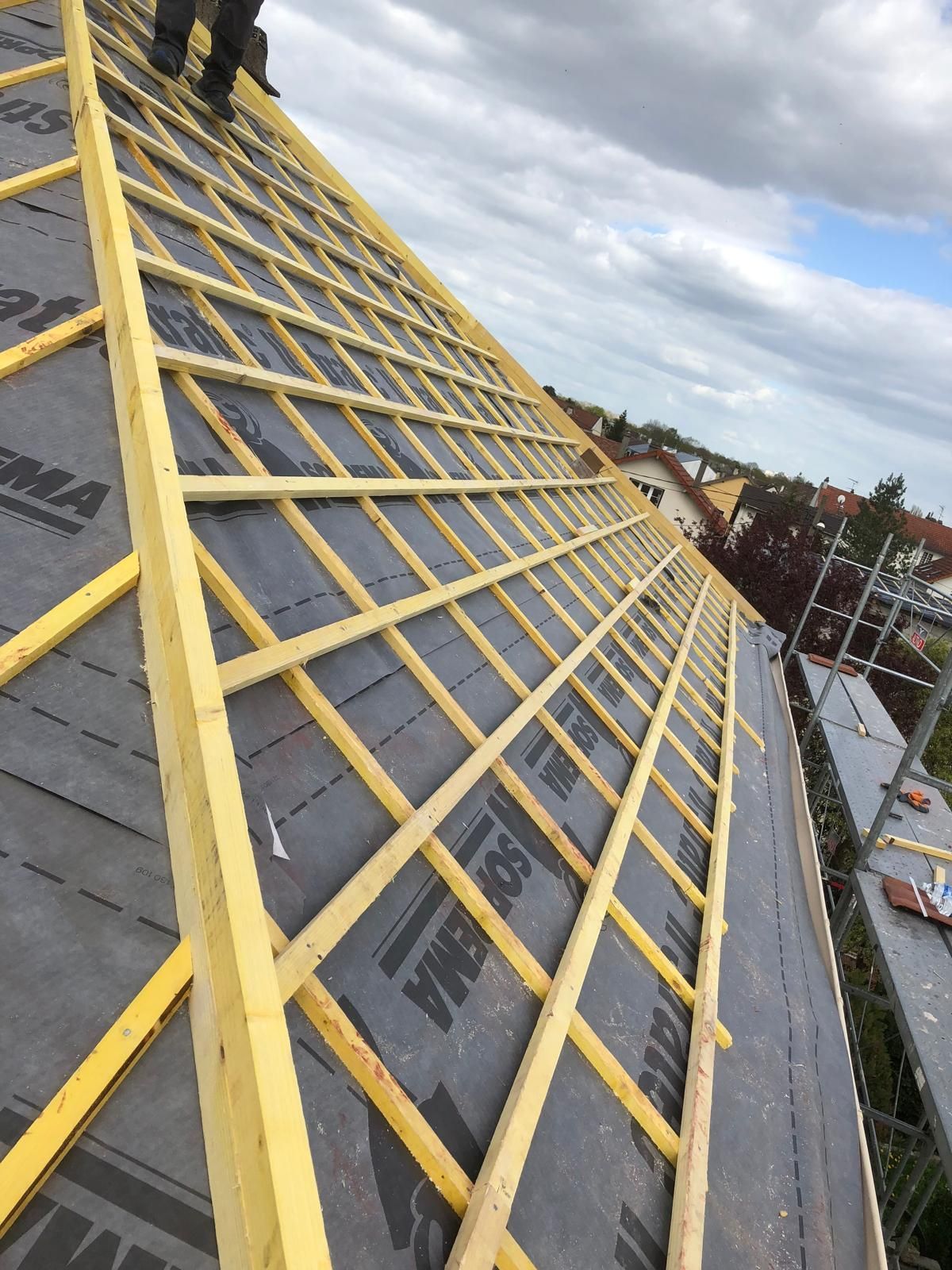 Lattes de toiture jaunes recouvrant une membrane d'étanchéité sombre sur le toit pentu d'une maison sous un ciel nuageux