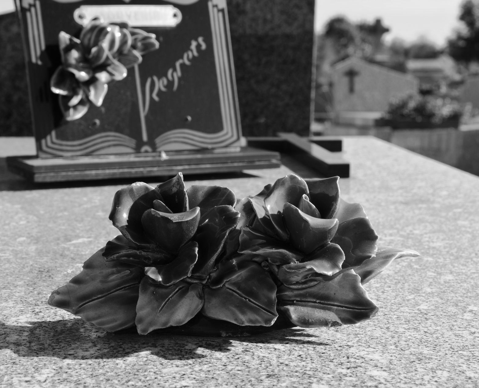 Roses en céramique sur une pierre tombale, avec une pierre tombale en arrière-plan dans un cimetière.