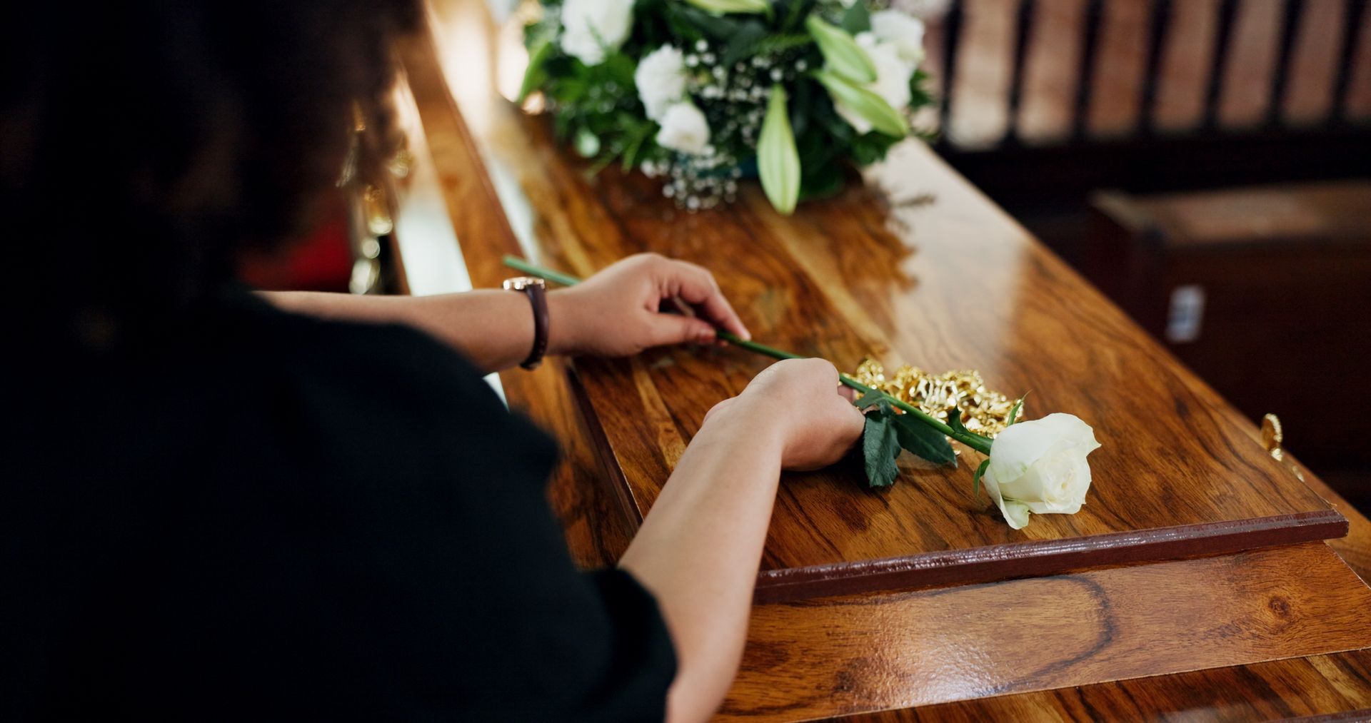 Personne déposant une rose blanche sur un cercueil en bois, probablement lors d'un service funèbre.