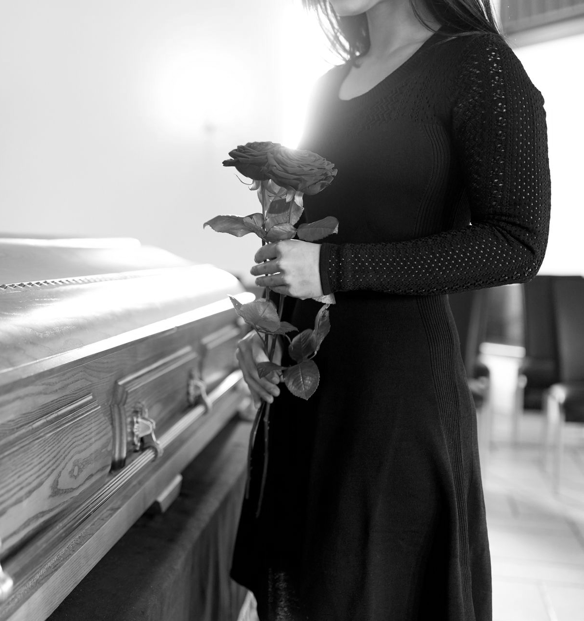 Une femme en noir tenant une rose rouge dans un cercueil dans une maison funéraire.