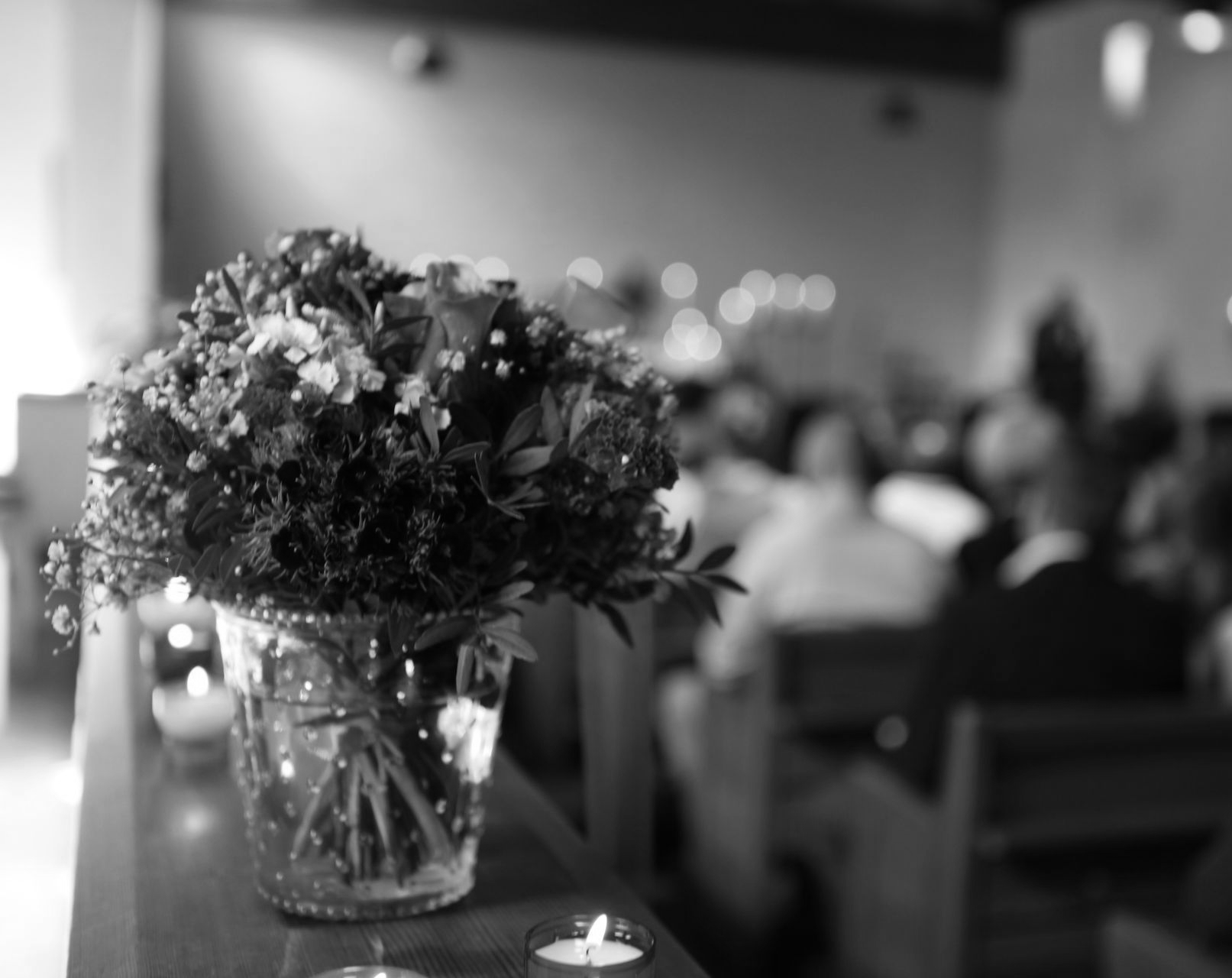 Vase de fleurs colorées et bougies allumées sur un banc d'église, arrière-plan flou de personnes.