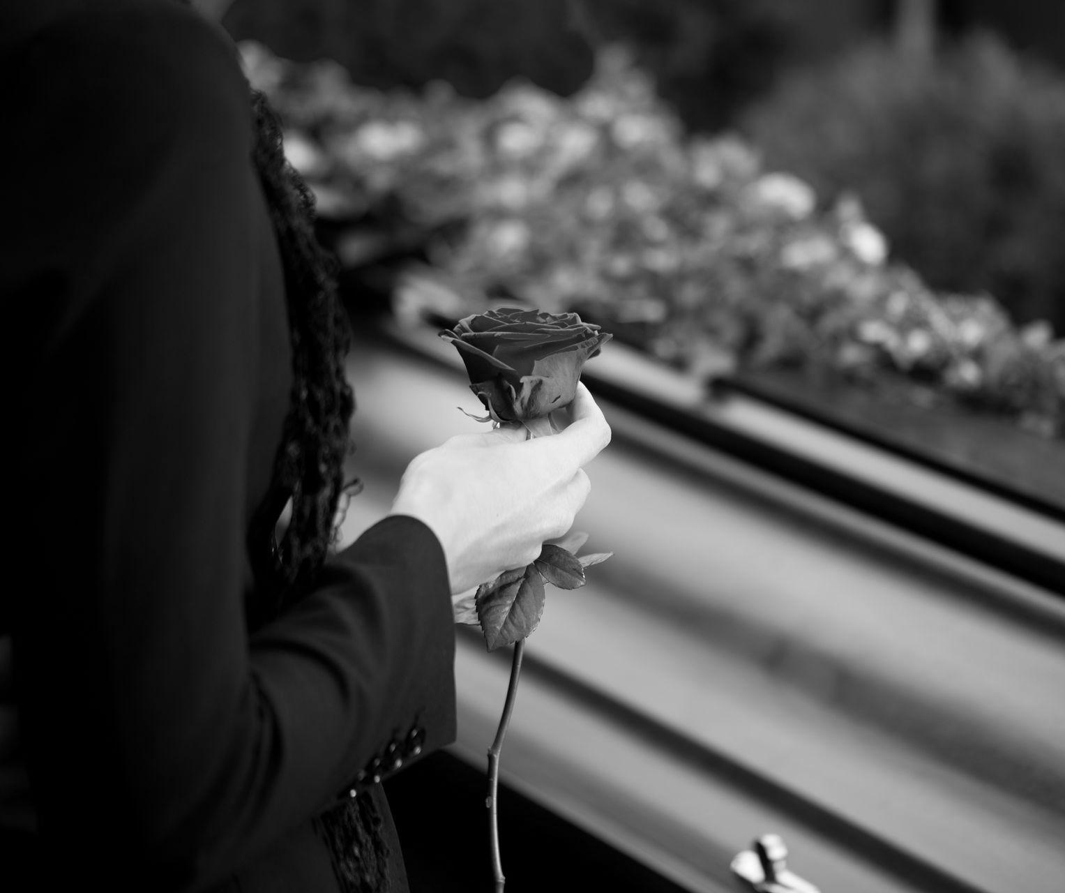Personne en noir, tenant une rose rouge près d'un cercueil, lors d'un enterrement.