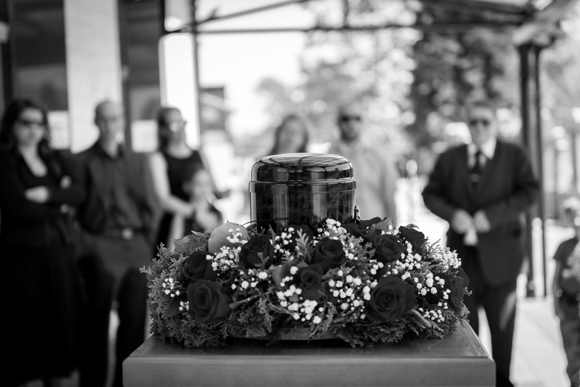 Une urne en bois avec des roses rouges et des personnes en deuil lors d'un enterrement.