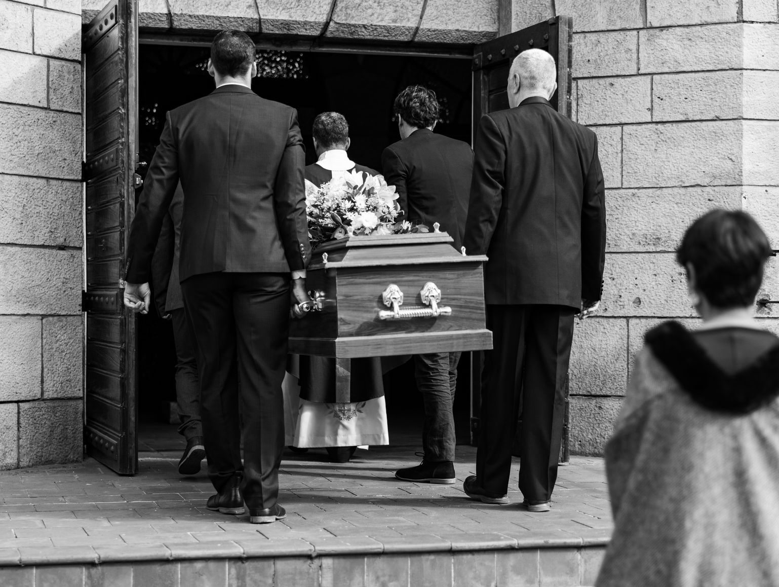Des porteurs transportent un cercueil hors d'une église, tandis que des personnes en deuil regardent.