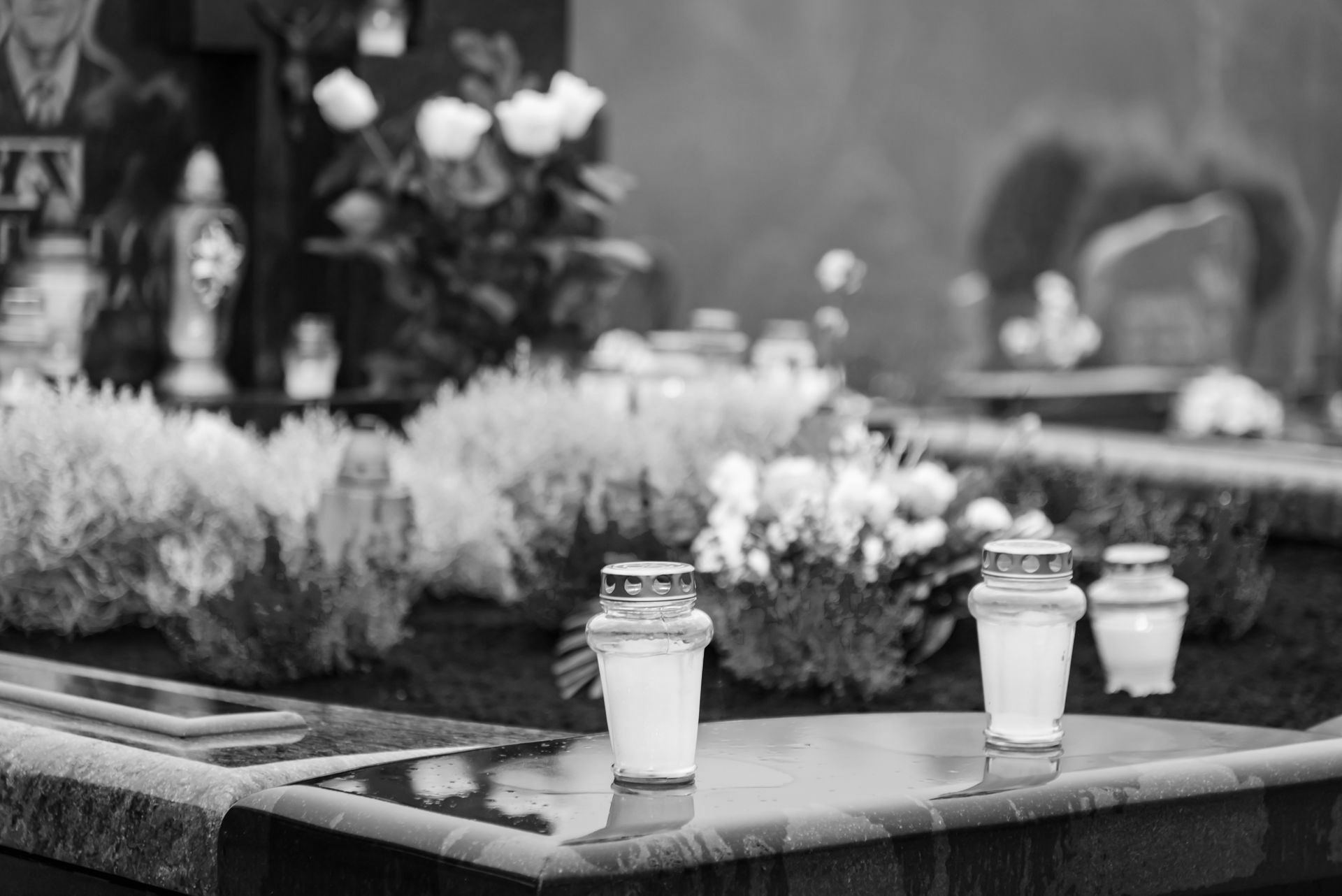 Scène de cimetière : tombes avec bougies, fleurs colorées et roses blanches dans des vases ; journée nuageuse.