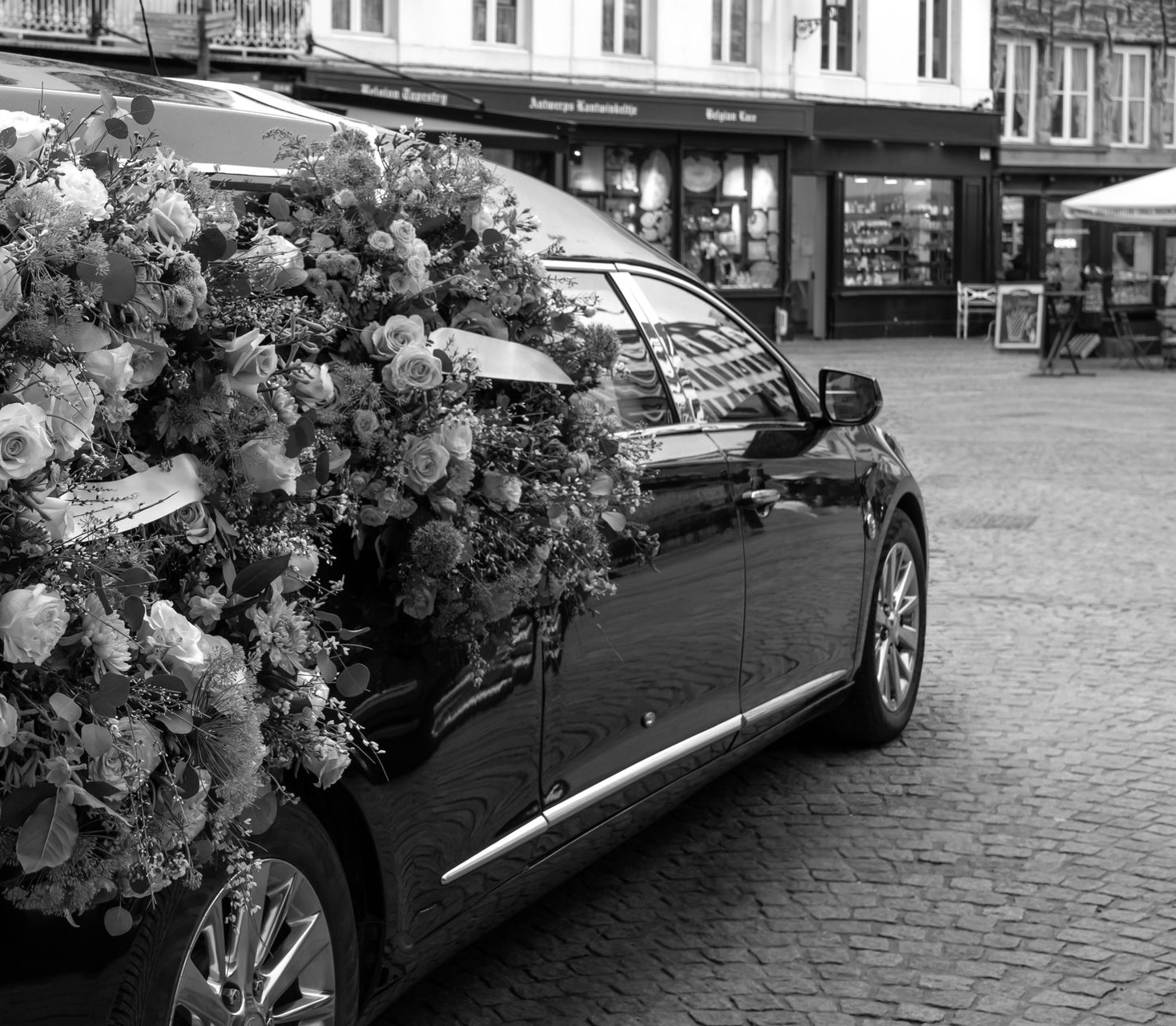 Voiture noire richement décorée de fleurs colorées, garée dans une rue pavée.