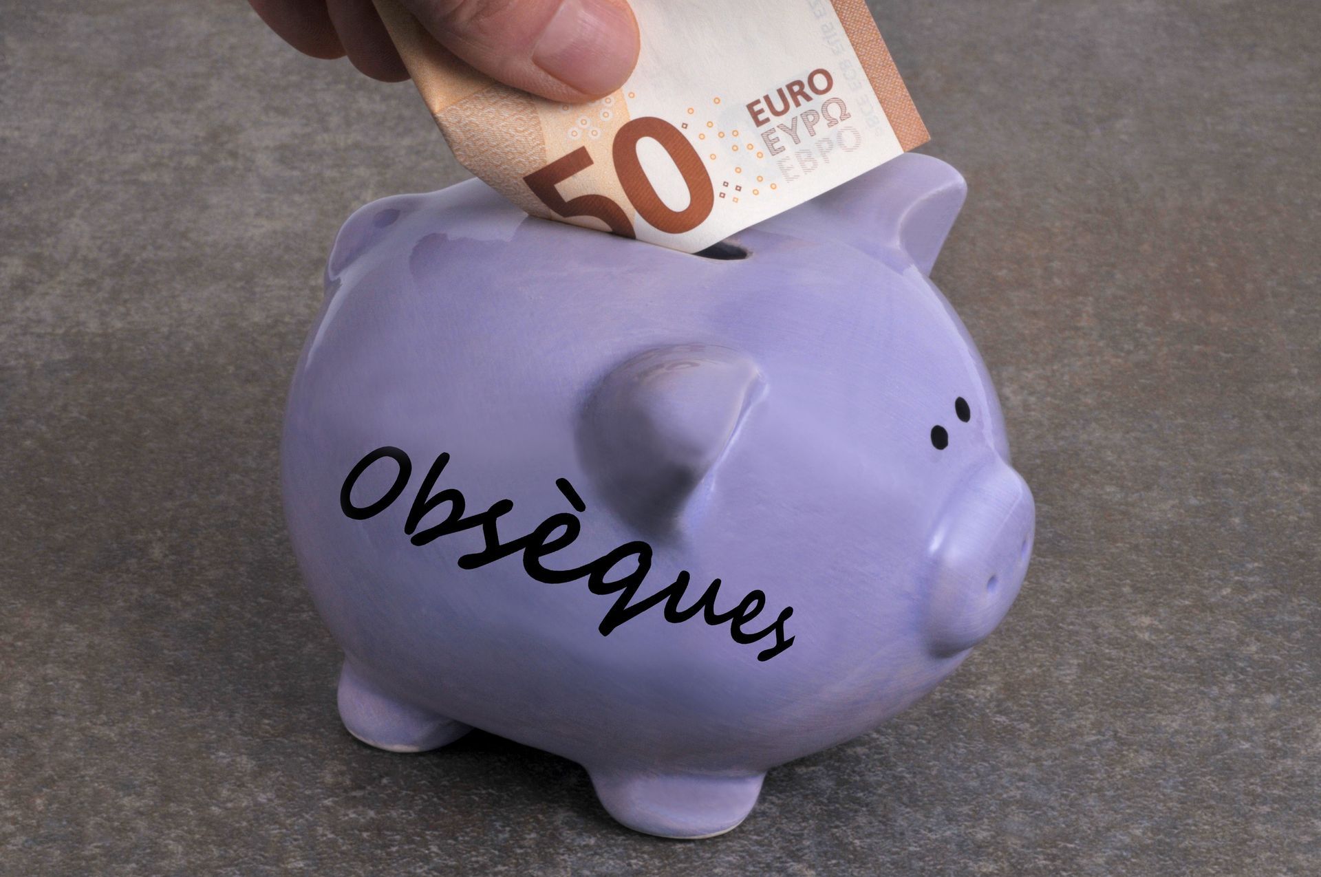 Main mettant un billet de 50 euros dans une tirelire violette étiquetée Obsèques.
