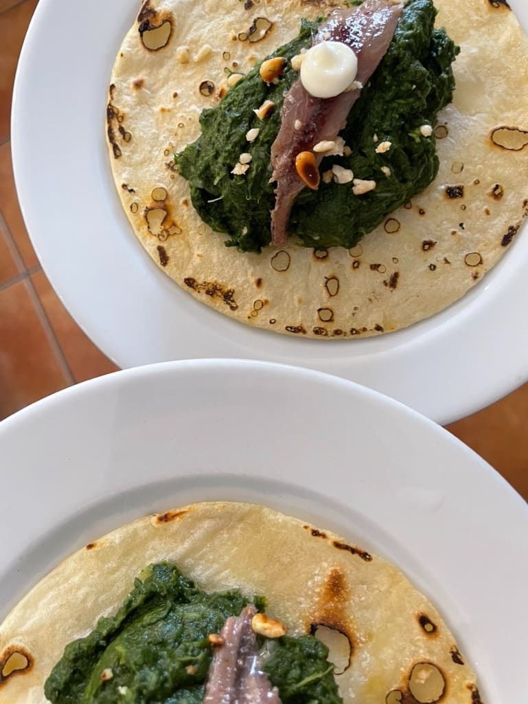 Dos panes planos tipo crepe en platos blancos con relleno verde y una cucharada de salsa blanca.