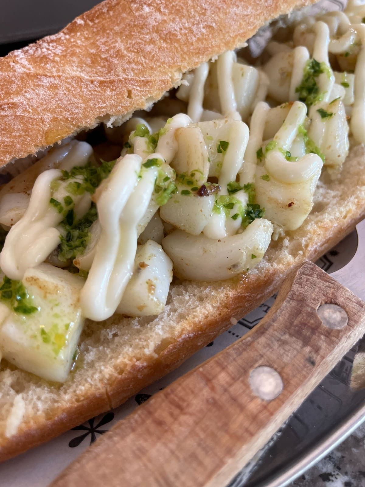 Primer plano de un bocadillo de baguette relleno de queso blanco o crema y pesto verde, en un plato con un cuchillo.