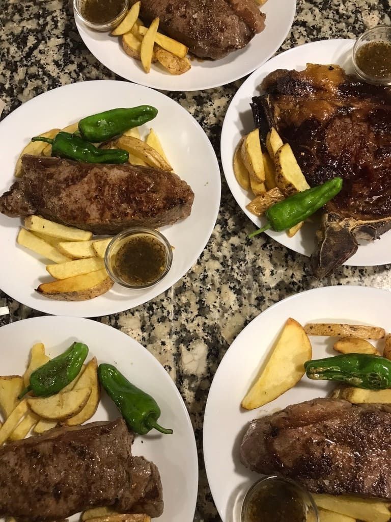 Platos de bistec con papas asadas y pimientos verdes sobre una encimera moteada.