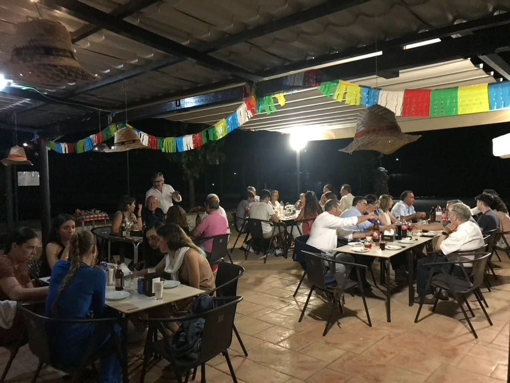 Zona de comedor al aire libre en el patio con gente sentada en mesas bajo coloridas guirnaldas y luces brillantes.