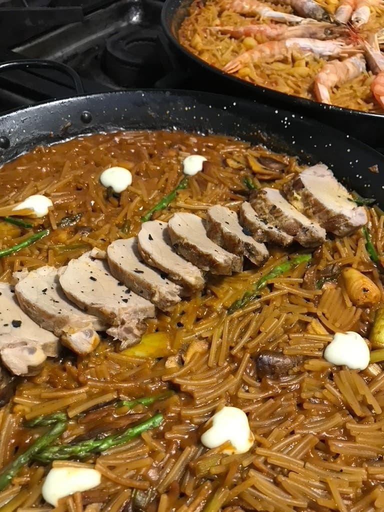 Pollo en rodajas sobre arroz integral en sartén con salsa blanca y judías verdes; paellera al fondo.