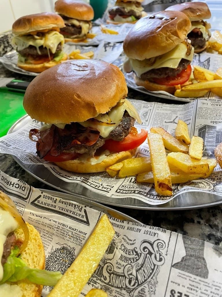 Hamburguesas emplatadas con patatas fritas en bandejas estilo periódico en una mesa de restaurante informal.