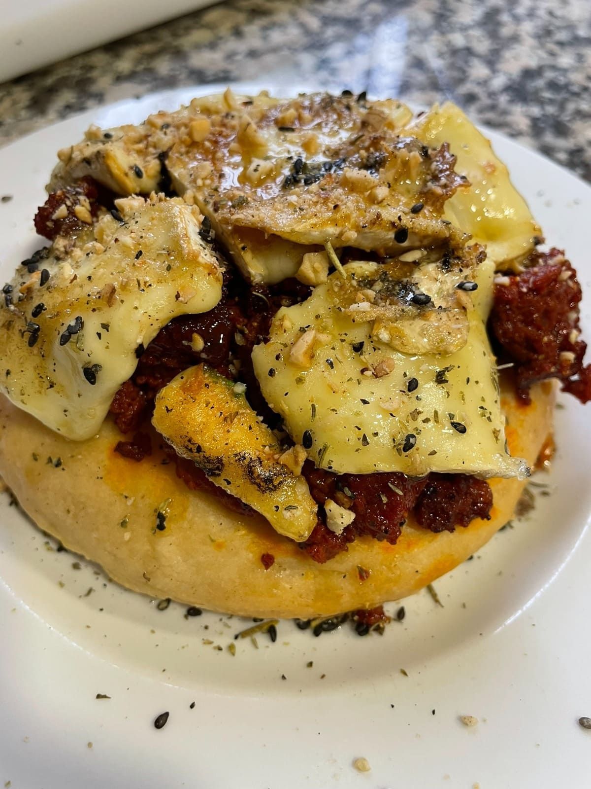 Sándwich abierto con queso fundido, carne y hierbas en un plato blanco.