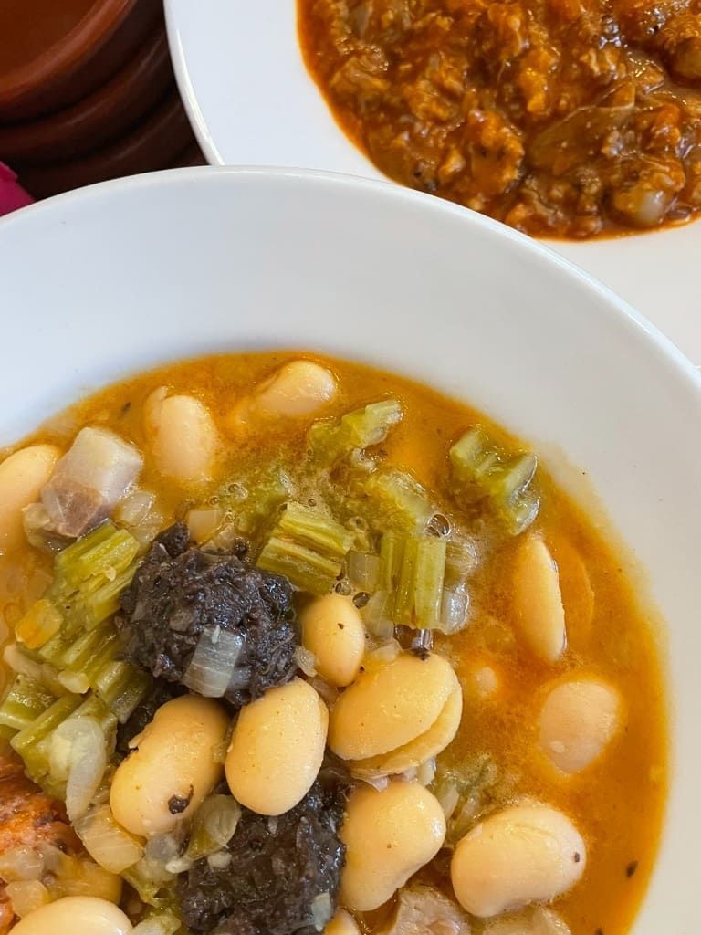 Tazones de sopa de frijoles con verduras y carne en un tazón blanco, servidos junto a otro plato parecido a un guiso.