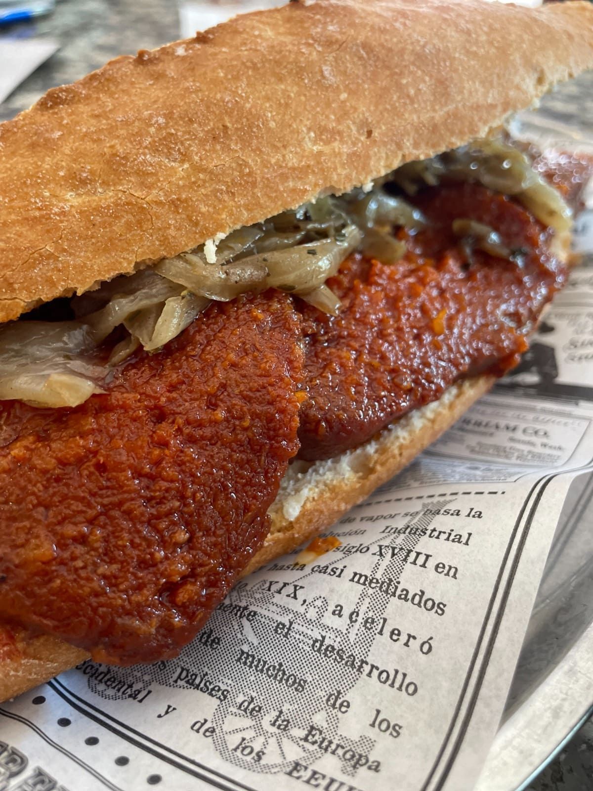 Primer plano de un sándwich frito empanizado con cebollas encurtidas sobre papel impreso con textura de periódico.