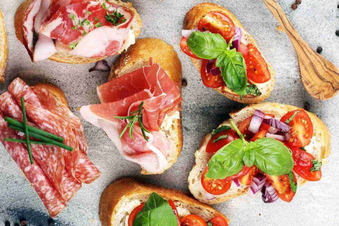 Variedad de crostini gourmet y bocaditos de antipasto con prosciutto, tomates y albahaca sobre una superficie de piedra.