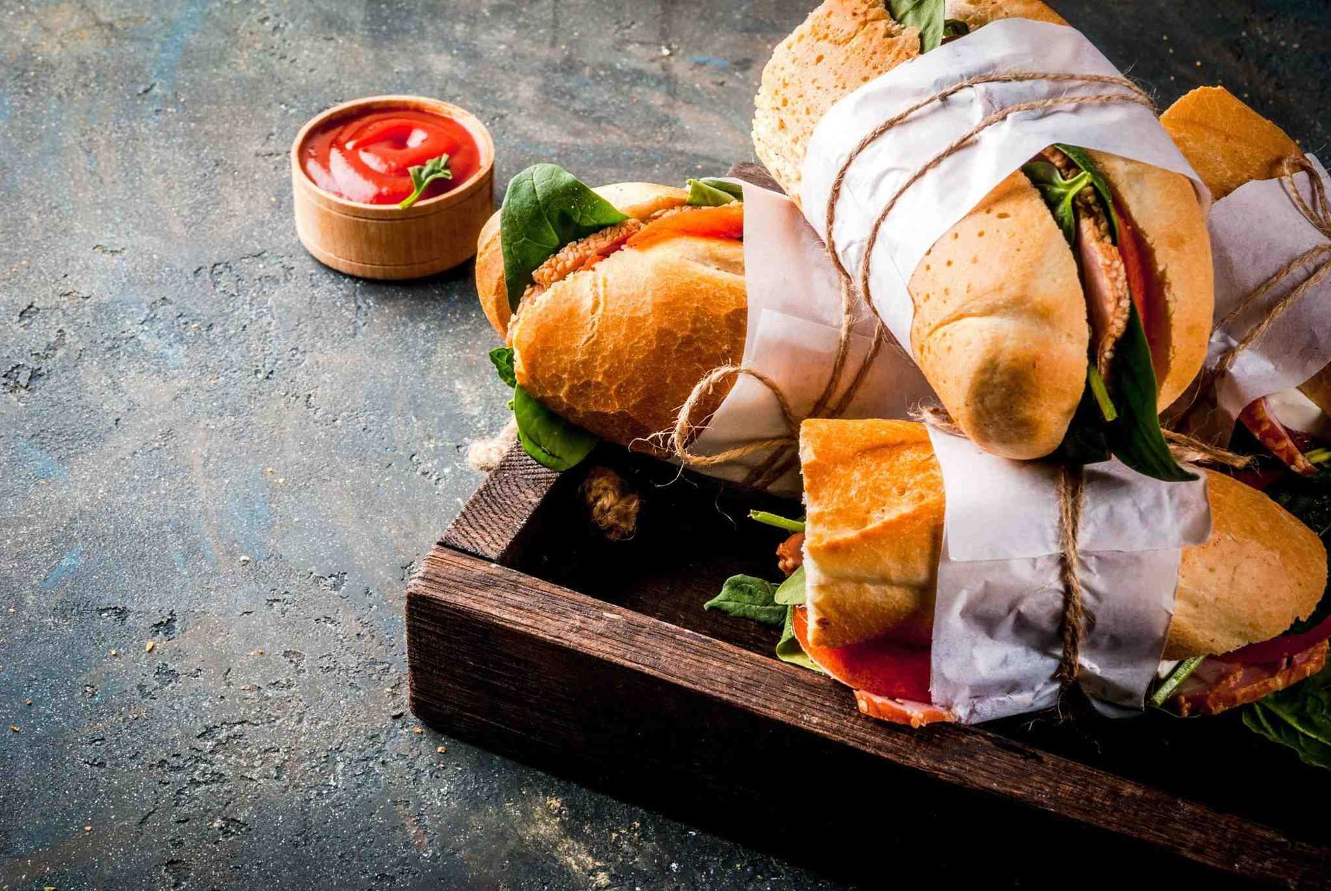 Sándwiches envueltos y salsa para mojar sobre una tabla de madera oscura.