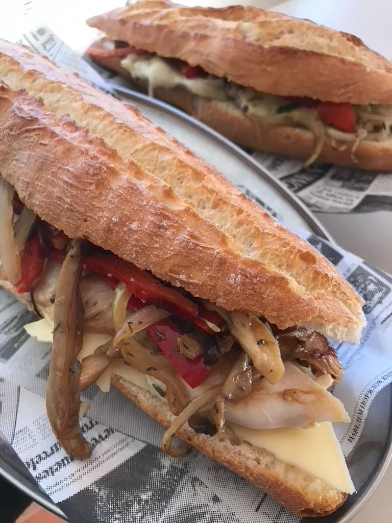 Dos sándwiches largos sobre papel, rellenos de verduras a la parrilla y queso sobre una mesa.