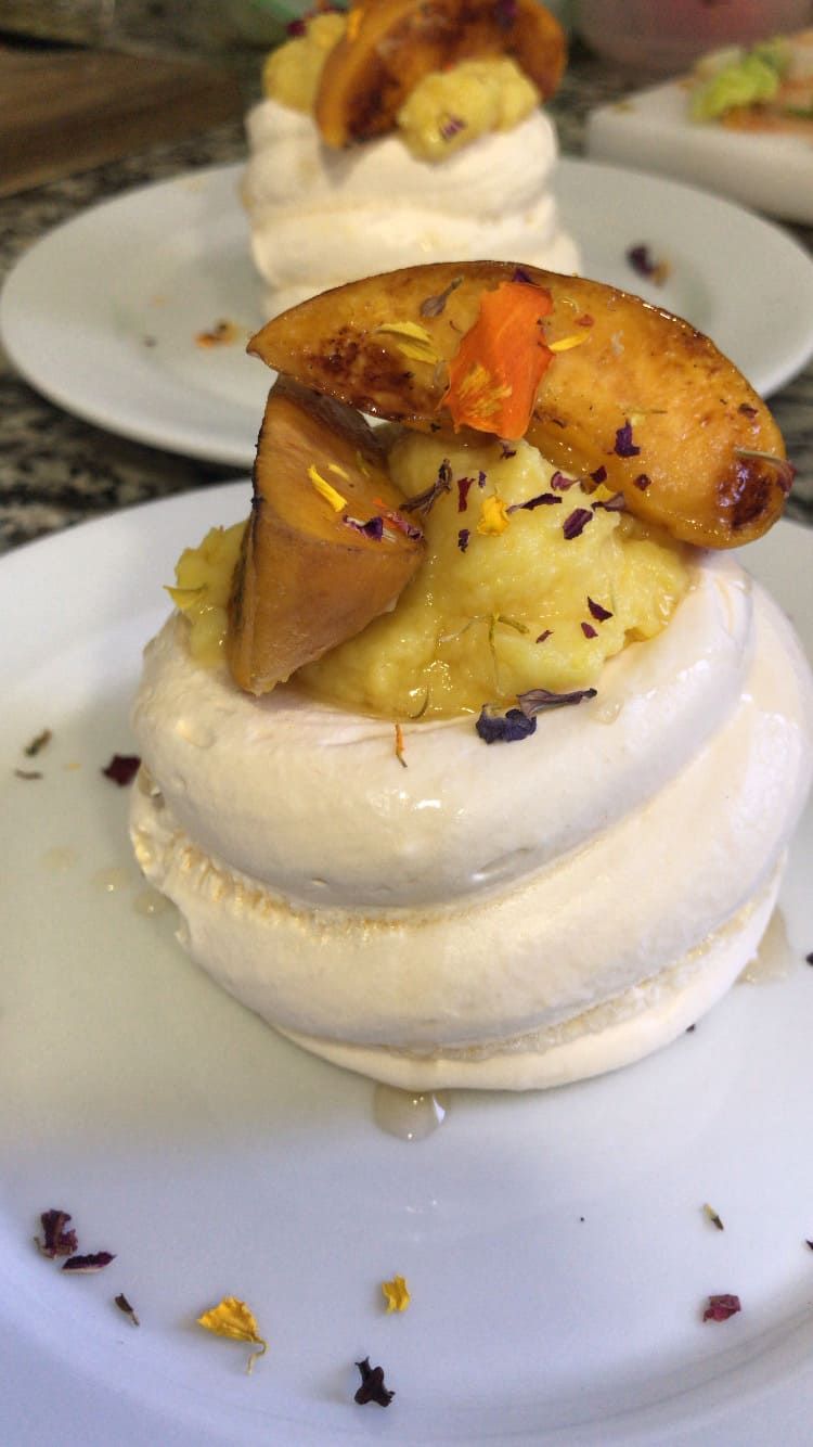 Mini pavlova cubierta con fruta caramelizada en un plato blanco con salsa rociada.