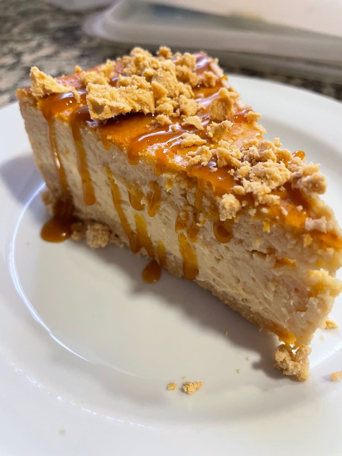 Porción de tarta de queso con sirope de caramelo y cobertura de migas sobre un plato blanco.