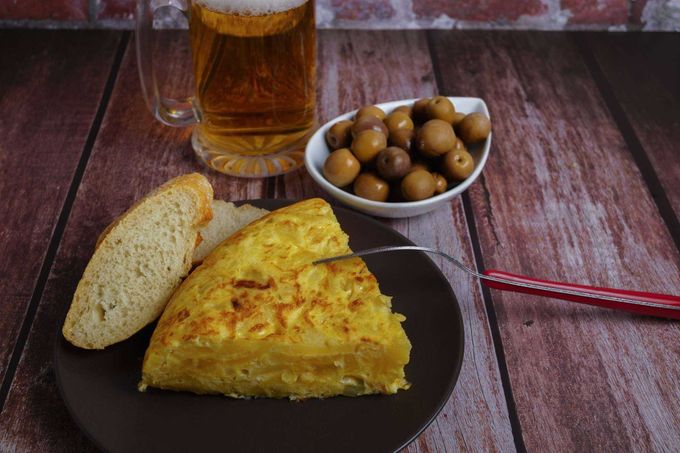 Desayuno turco con tortilla, pan, aceitunas y un vaso de té en una mesa rústica de madera.