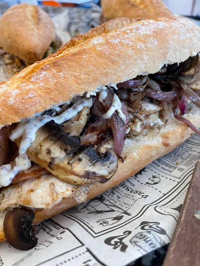 Sándwich a la plancha con queso fundido y cebolla en una bandeja forrada con papel.