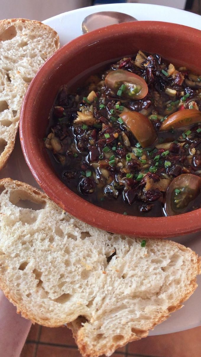 Rebanadas de pan rústico alrededor de un pequeño cuenco de tapenade de aceitunas negras con hierbas y aceitunas.